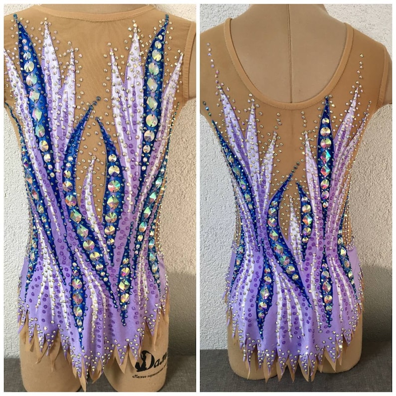 May include: A purple, white, and blue leotard with a geometric design. The leotard is decorated with rhinestones and has a mesh back.