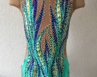 May include: A turquoise leotard with a geometric design featuring blue and purple rhinestones. The leotard has a scoop neck and sleeveless design.