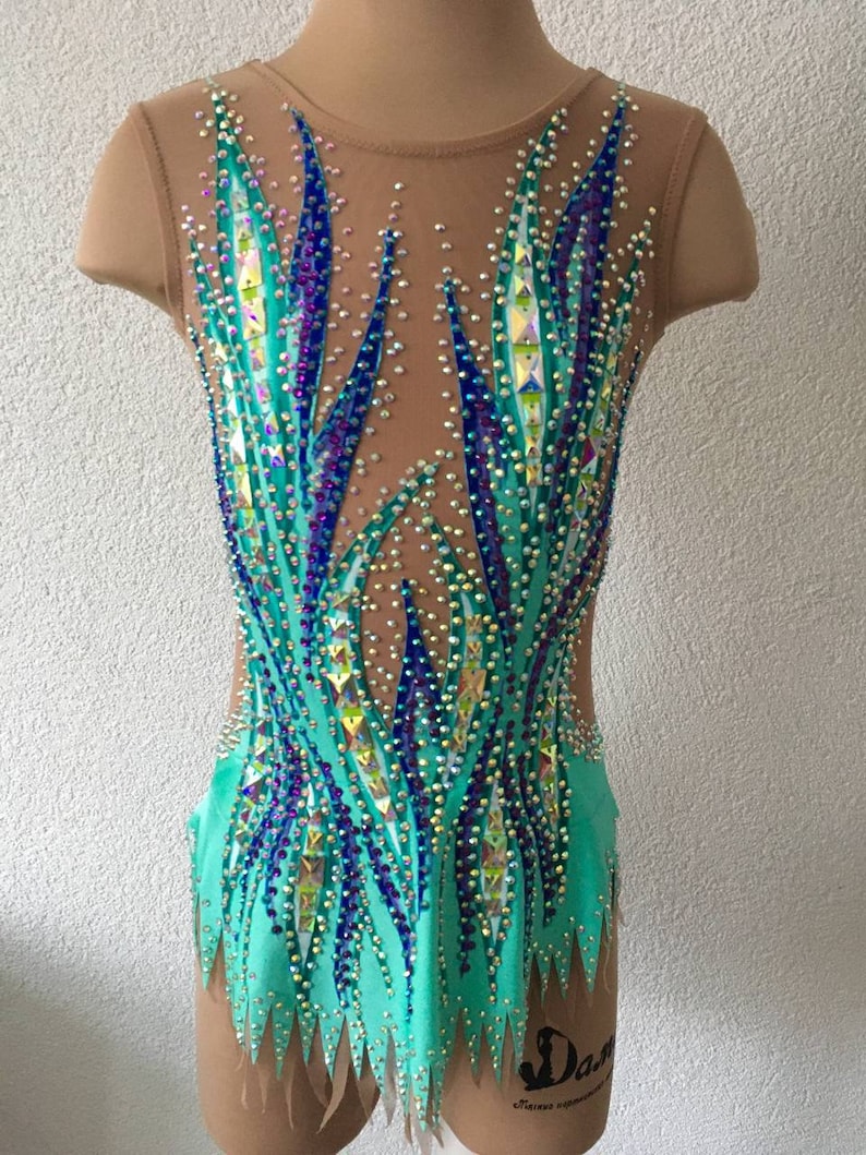 May include: A turquoise leotard with a geometric design featuring blue and purple rhinestones. The leotard has a scoop neck and sleeveless design.