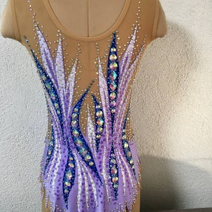 May include: A purple and blue leotard with a geometric design. The leotard is decorated with rhinestones and has a scalloped hem.