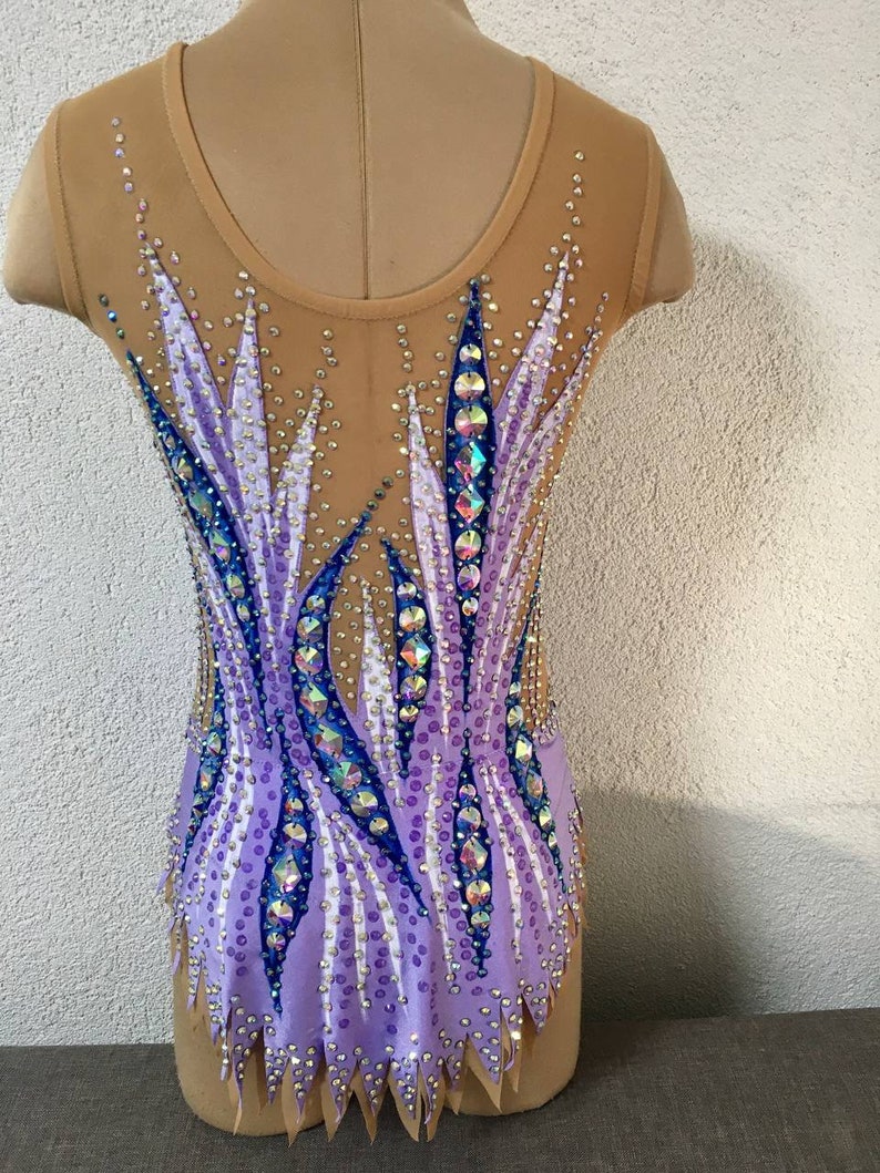 May include: A purple and blue leotard with a geometric design. The leotard is decorated with rhinestones and has a scalloped hem.