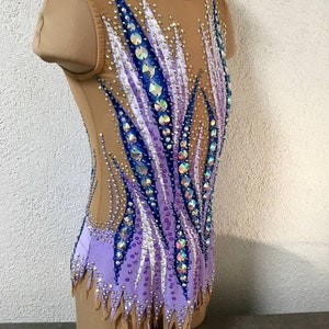 May include: A purple, blue, and white leotard with a flame design and rhinestones. The leotard has a scoop neck and sleeveless design.