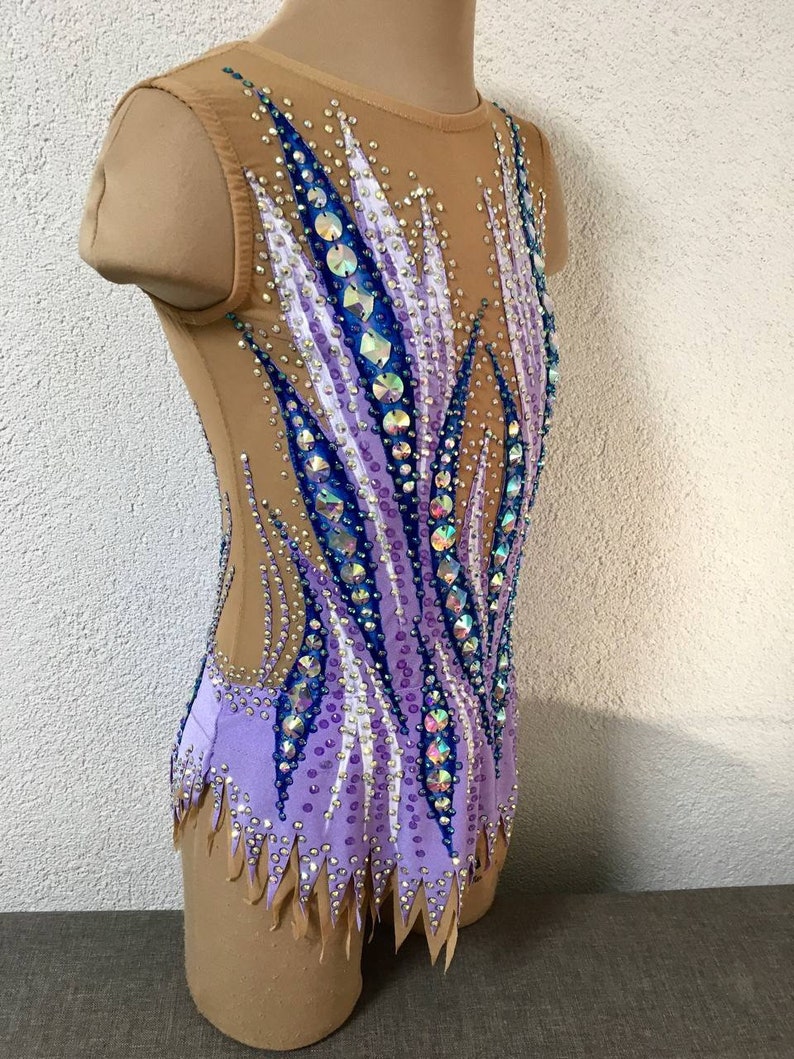 May include: A purple, blue, and white leotard with a flame design and rhinestones. The leotard has a scoop neck and sleeveless design.