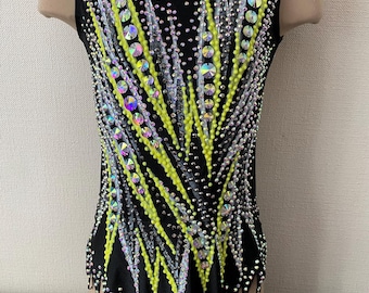 Può includere: Body nero con un vivace design di strass gialli e iridescenti. L'indumento senza maniche presenta un motivo dettagliato di abbellimenti scintillanti, creando un effetto abbagliante. Il body è progettato per la ginnastica o la danza.