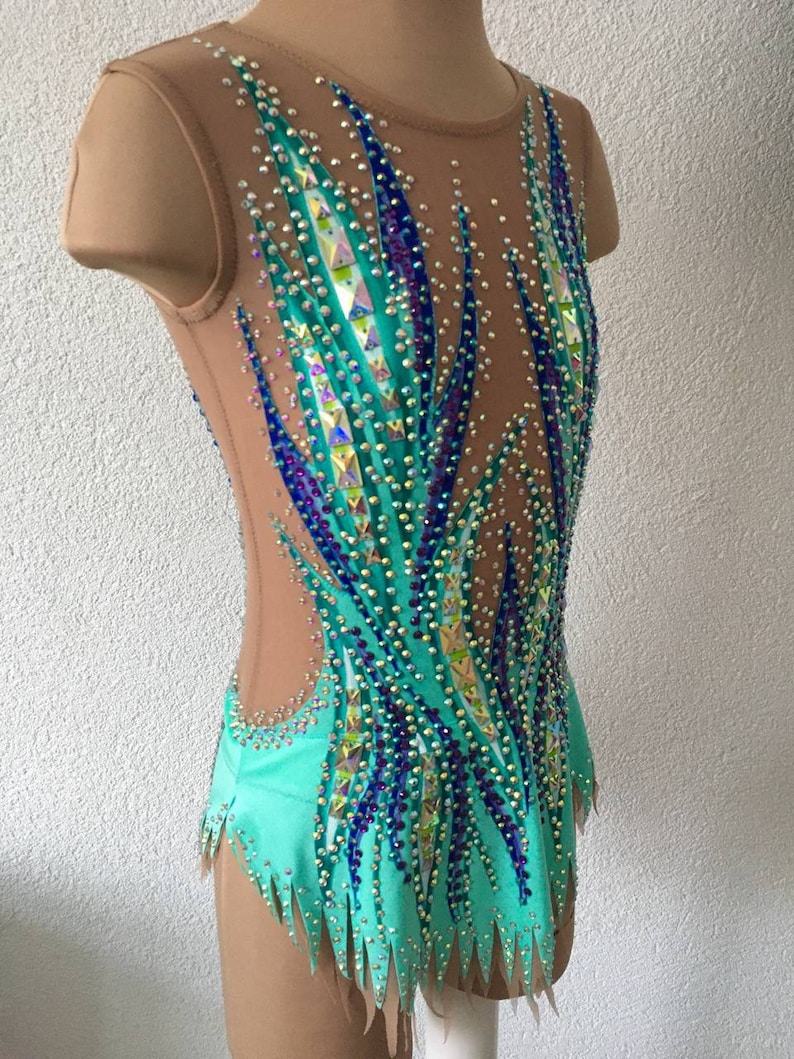 May include: A turquoise leotard with a sheer mesh overlay and a design of blue and green flames. The leotard is embellished with rhinestones.