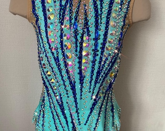 May include: A turquoise leotard with a mesh neckline and back, adorned with dark blue and iridescent rhinestones. The design features a feather-like pattern, creating a sparkling effect. This rhythmic gymnastics garment is displayed on a mannequin.