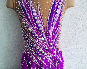 Può includere: Un body viola senza maniche con una sezione superiore in rete color carne, riccamente decorato con strass e cristalli. Il design presenta un motivo a forma di V sul davanti e sul retro, con un orlo a zig-zag. Il body è progettato per la ginnastica ritmica.