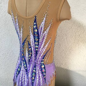 May include: A purple and white leotard with a geometric design and rhinestones. The leotard has a scoop neck and sleeveless design.
