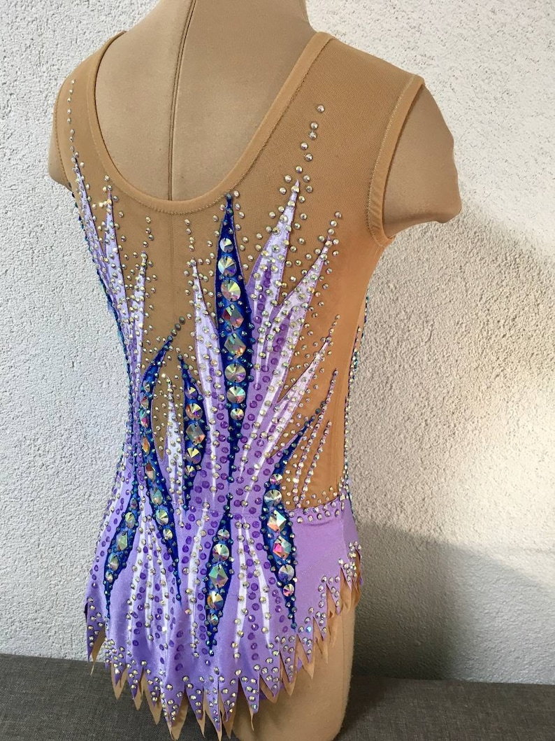 May include: A purple and white leotard with a geometric design and rhinestones. The leotard has a scoop neck and sleeveless design.
