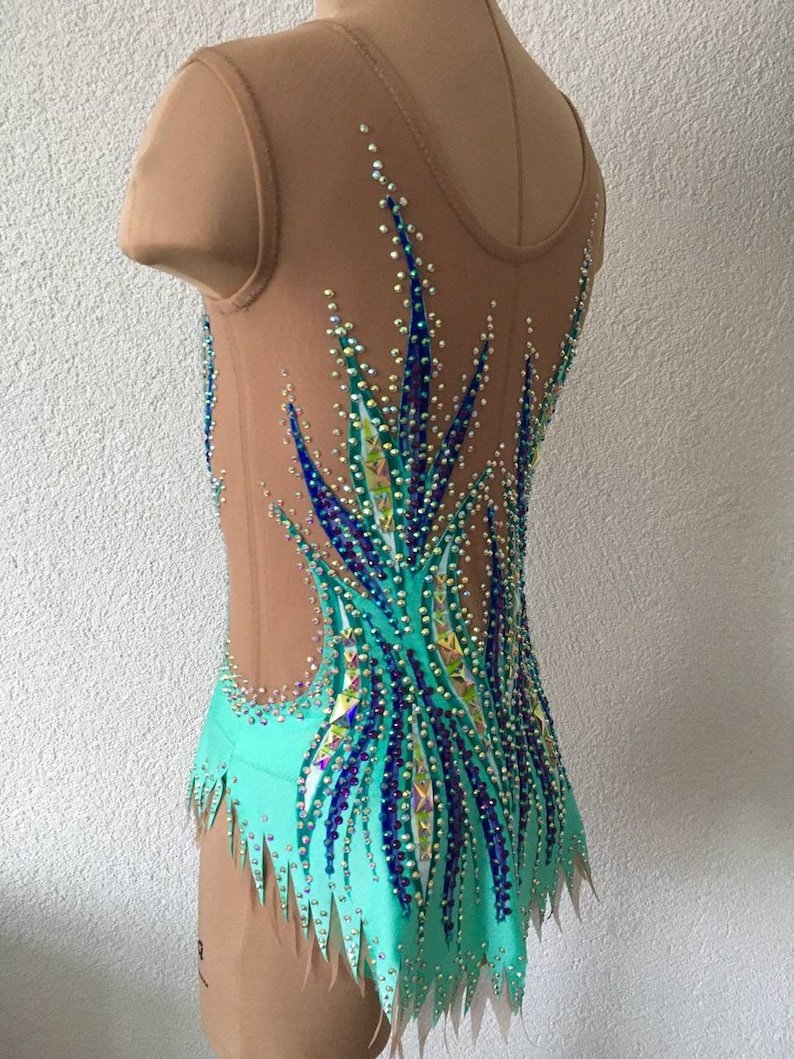 May include: A turquoise leotard with a sheer bodice and a design of blue and green rhinestones. The leotard has a jagged hemline.