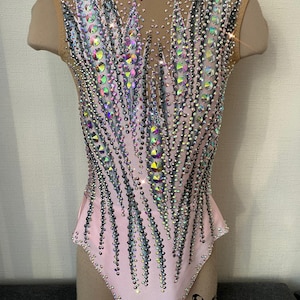 May include: A light pink leotard with a nude mesh upper back and shoulders. The leotard is heavily embellished with iridescent rhinestones and crystals, arranged in a feather-like pattern. The design is symmetrical, with the embellishments cascading down the front and back.