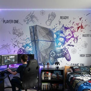 Könnte beinhalten: Ein Gaming-Zimmer mit einem Wandbild, das eine Konsole und einen Controller zeigt. Der Raum verfügt über einen Schreibtisch mit mehreren Bildschirmen, einen Gaming-Stuhl und ein Bett mit einem Bettbezug im Controller-Design. Poster und Regale mit Spielen vervollständigen das Setup.