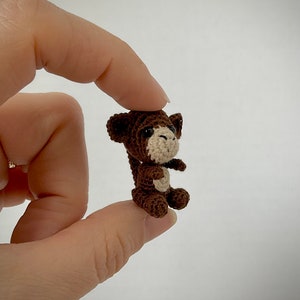 May include: A small brown crocheted monkey with a white face and black eyes. The monkey is sitting with its arms crossed and its legs bent.