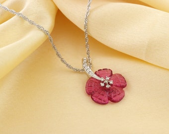 May include: A silver necklace featuring a pendant shaped like a five-petaled flower. The flower is crafted from a deep pink, translucent material with a faceted surface. A silver bail set with small clear stones connects the flower to a silver chain.