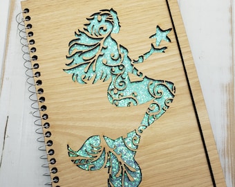 May include: A wooden spiral bound journal with a teal glitter mermaid design cut out of the front cover.