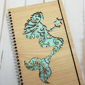May include: A wooden spiral bound journal with a teal glitter mermaid design cut out of the front cover.