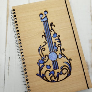 May include: A wooden spiral bound notebook with a blue glitter guitar design. The guitar is cut out of the wood and the glitter is in the cut out area.