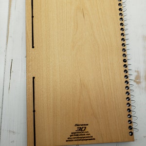 May include: A wooden spiral bound notebook with a black elastic closure and the text "Genesis 3D" and contact information printed on the back cover.