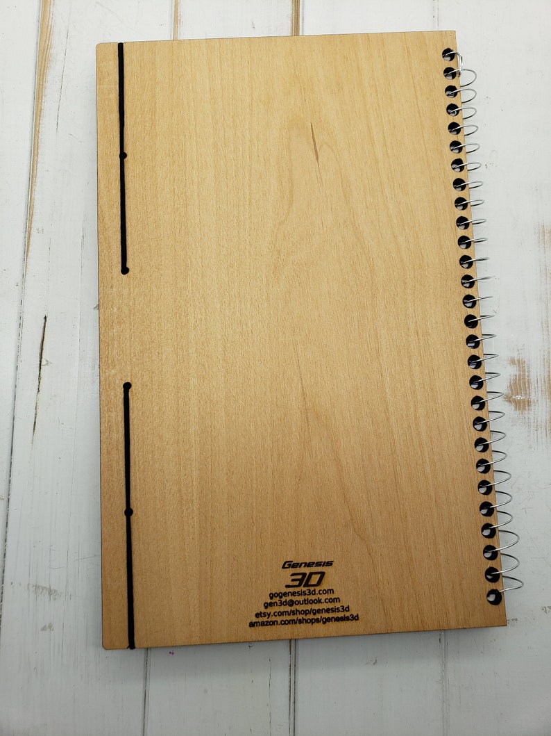 May include: A wooden spiral bound notebook with a black elastic closure and the text "Genesis 3D" and contact information printed on the back cover.