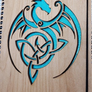 May include: A wooden journal with a spiral binding and a turquoise blue dragon design carved into the front cover.