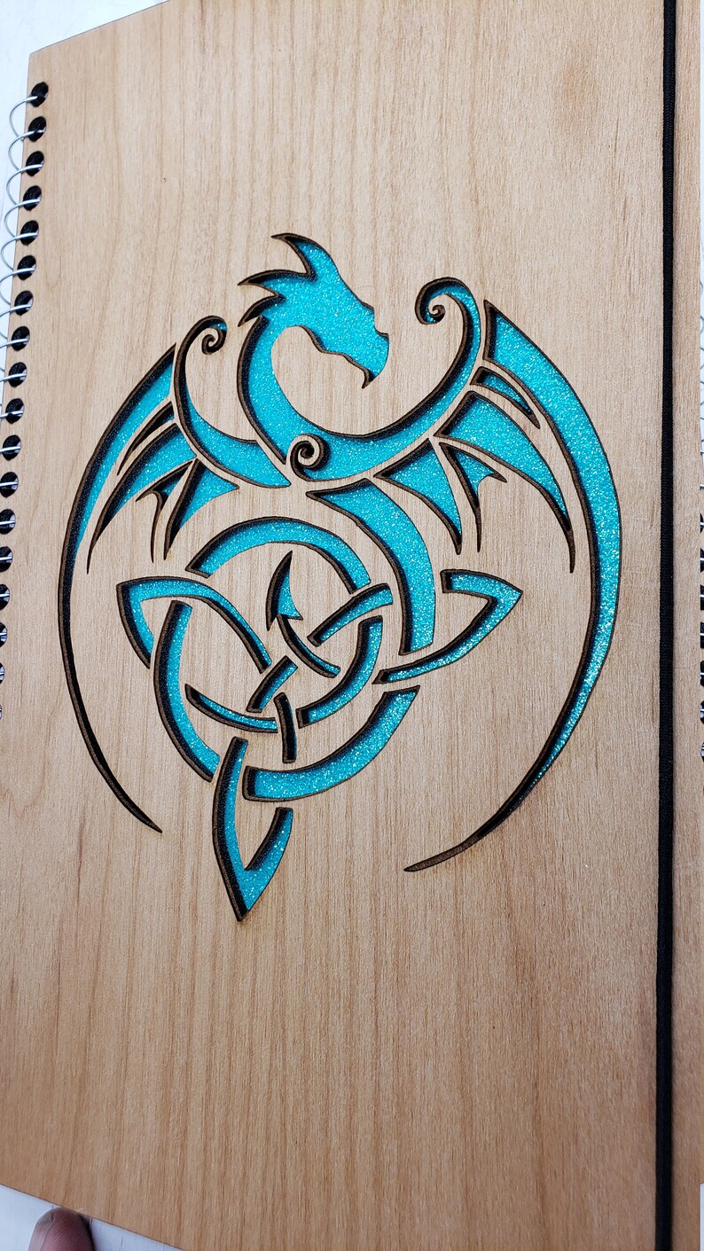 May include: A wooden journal with a spiral binding and a turquoise blue dragon design carved into the front cover.