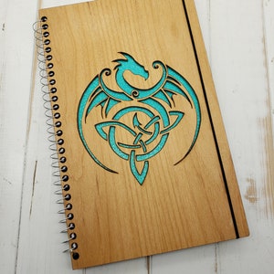 May include: A wooden spiral bound notebook with a teal blue Celtic knot and dragon design.