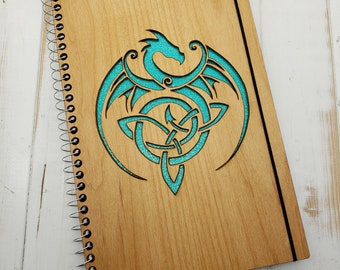 May include: A wooden spiral bound notebook with a teal blue Celtic knot and dragon design.