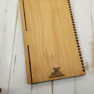 May include: A wooden spiral bound notebook with a wood grain pattern. The back cover has the text "Genesis 3D" and contact information for the company.