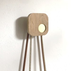 Peut inclure: Une étagère murale en bois avec une découpe circulaire et trois chaînes suspendues. L'étagère est de couleur brun clair et les chaînes sont dorées.