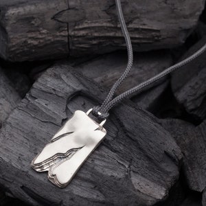 Op de afbeelding: Een zilveren ketting met een unieke, abstracte hanger. De hanger is gevormd als een grillige, gelaagde bergketen. De ketting is aan een grijs koord.