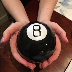 Pode incluir: Uma bola m&aacute;gica preta com o n&uacute;mero oito branco nela.