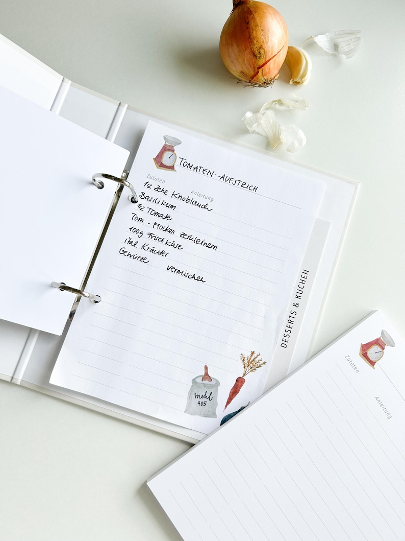 May include: A white binder with a recipe page for tomato spread. The page has a handwritten list of ingredients and instructions. The page is decorated with a watercolour illustration of a scale and a bag of flour.