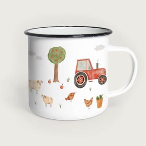 Könnte beinhalten: Weißer Emaillebecher mit schwarzem Rand, mit einer Aquarellillustration eines roten Traktors, Schafen, Hühnern, einem Apfelbaum und Äpfeln. Das Design hat ein Bauernhof-Thema.