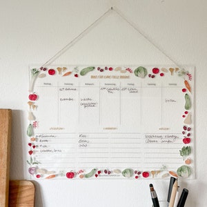 Peut inclure: Un planificateur hebdomadaire en acrylique transparent avec un motif aquarelle de fruits et légumes. Le planificateur comporte des sections pour le lundi au dimanche, avec de l'espace pour écrire des rendez-vous, des tâches et des notes. Le planificateur comporte également des sections pour la planification des repas, les courses et les notes.