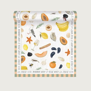 Op de afbeelding: Opgerolde witte stof met een kleurrijk patroon van fruit, zeevruchten en een zeemeeuw. De rand heeft een groen en perzik streepontwerp met de tekst "LA DOLCE VITA MAMMA MIAI O SOLE MIOI LA DOLCE VITA".
