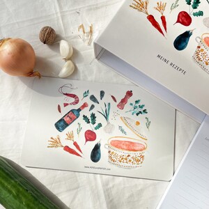 May include: A watercolour illustration of a pot of soup with various ingredients, including carrots, aubergine, garlic, wine, and herbs. The illustration is on a white card with the text "www.HERZundPAPIER.com" at the bottom. The card is on a white surface.
