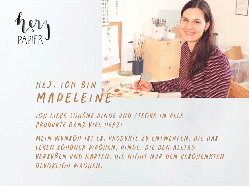 May include: A woman sits at a table with art supplies and paints. The text "HEJ, ICH BIN MADELEINE" is written in brown lettering. The text "ICH LIEBE SCH&Ouml;NE DINGE UND STECKE IN ALLE PRODUKTE GANZ VIEL HERZ!" is written in brown lettering. The text "MEIN WUNSCH IST ES, PRODUKTE ZU ENTWERFEN, DIE DAS LEBEN SCH&Ouml;NER MACHEN. DINGE, DIE DEN ALLTAG VERS&Uuml;BEN UND KARTEN, DIE NICHT NUR DEN BESCHENKTEN GL&Uuml;CKLICH MACHEN." is written in brown lettering.