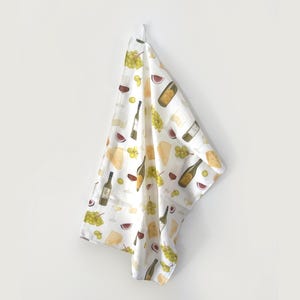 Könnte beinhalten: Weißes Küchentuch mit einem sich wiederholenden Muster aus Weinflaschen, Käsescheiben, Trauben und Weingläsern. Das Tuch hängt an einer weißen Wand. Das Design umfasst Farbtöne von Grün, Braun und Rot.