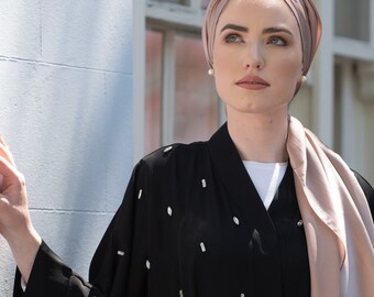 Könnte beinhalten: Eine Frau trägt einen schwarzen Abaya mit glitzernden Verzierungen. Sie trägt auch eine hellbraune Kopfbedeckung und einen passenden Schal. Der Abaya ist mit einem schwarzen Seilgürtel in der Taille zusammengebunden.