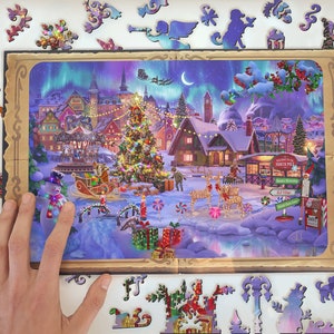 Pode incluir: Uma cena colorida de uma vila natalina com uma grande &aacute;rvore de Natal, casas cobertas de neve e um boneco de neve. A cena &eacute; iluminada com luzes brilhantes e cercada por uma moldura de madeira.
