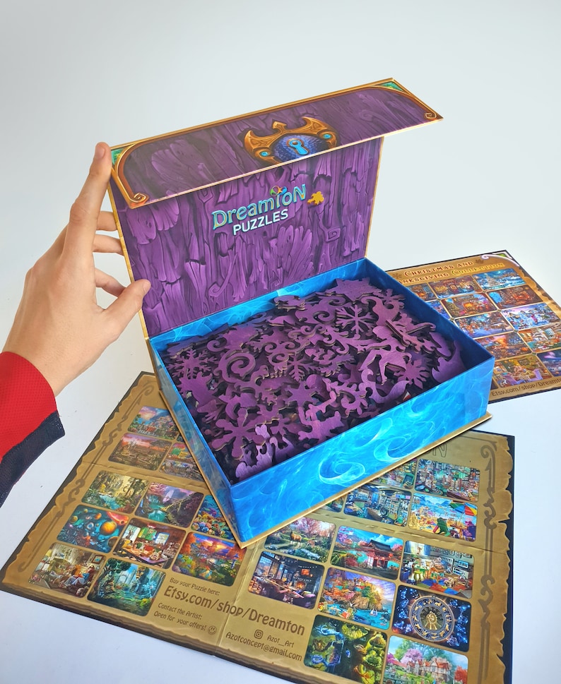 Pode incluir: Uma caixa de madeira roxa com uma tampa azul e dourada, aberta para revelar um quebra-cabe&ccedil;a de madeira com pe&ccedil;as intrincadas. A caixa tem o texto "Dreamion Puzzles" na frente. O quebra-cabe&ccedil;a &eacute; uma cena de Natal com uma variedade de edif&iacute;cios e personagens.