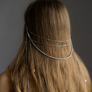 May include: A silver hair chain with crystal embellishments. The chain has three strands with dangling crystal drops.