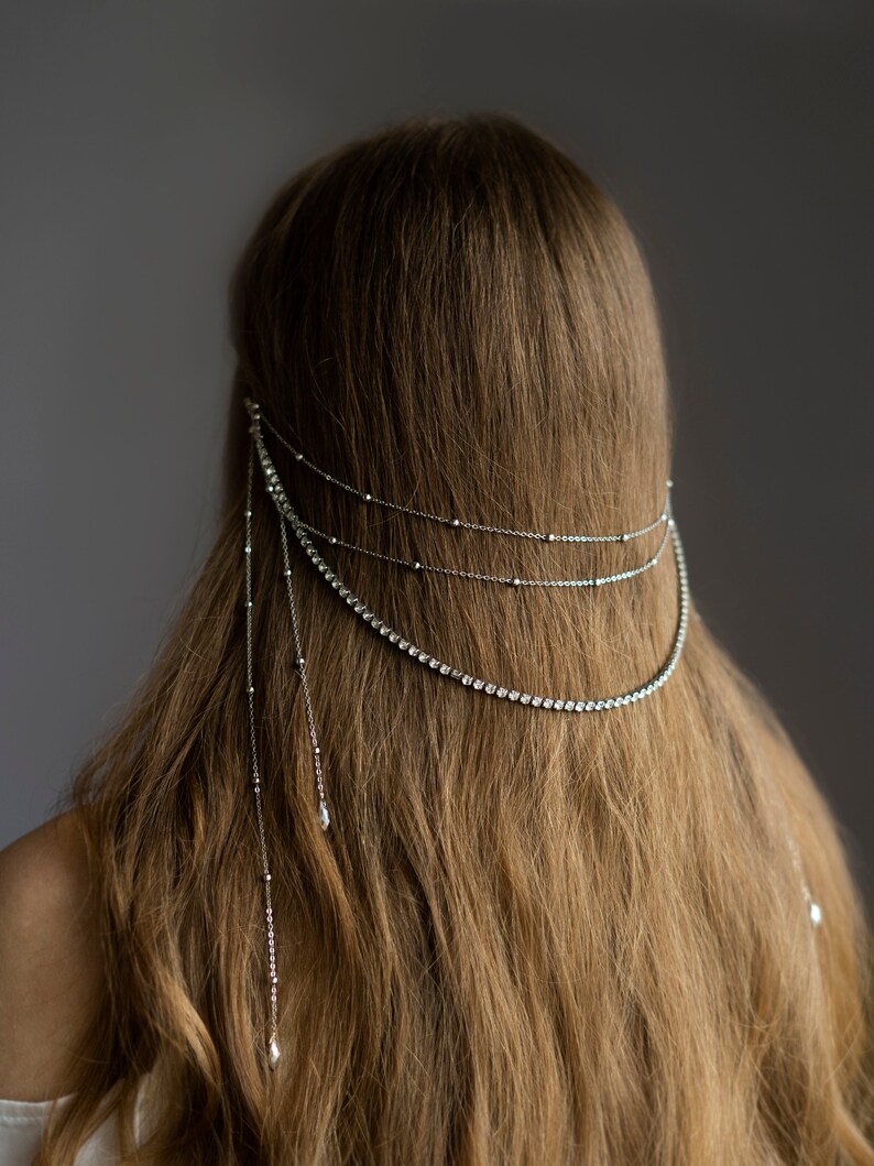 May include: A silver hair chain with crystal embellishments. The chain has three strands with dangling crystal drops.