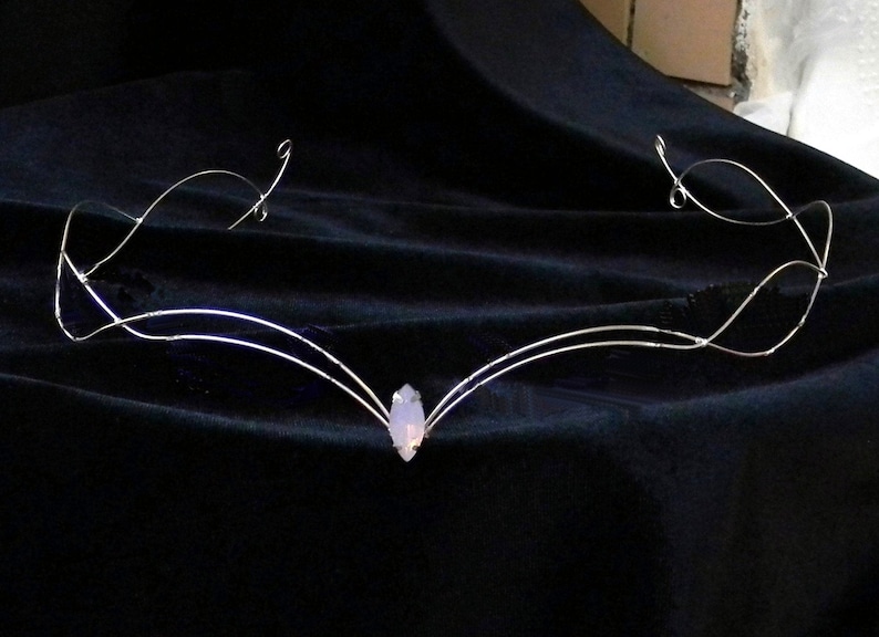 May include: A silver wire headband with a delicate, curved design and a single, pale purple gemstone in the center.