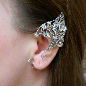 May include: Silver ear cuff with a floral design. The cuff features delicate leaves and flowers, and is designed to wrap around the ear.