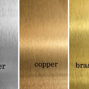 K&ouml;nnte beinhalten: Nahaufnahme von drei Metallproben mit geb&uuml;rsteten Oberfl&auml;chen. Die Proben sind mit "Silber", "Kupfer" und "Messing (Gold)" beschriftet.