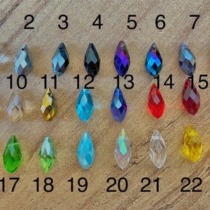 May include: A set of 23 teardrop-shaped crystal beads in various colors, including clear, red, blue, green, and yellow. The beads are numbered 1 through 23.