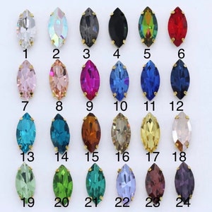 May include: Assortment of 24 marquise-shaped rhinestones in various colors, including clear, iridescent, black, red, pink, blue, green, gold, and brown. The rhinestones are arranged in four rows of six, with each rhinestone numbered 1 through 24.