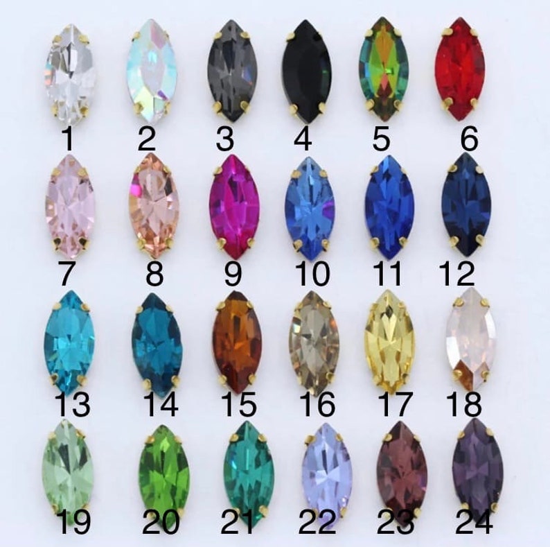 May include: Assortment of 24 marquise-shaped rhinestones in various colors, including clear, iridescent, black, red, pink, blue, green, gold, and brown. The rhinestones are arranged in four rows of six, with each rhinestone numbered 1 through 24.