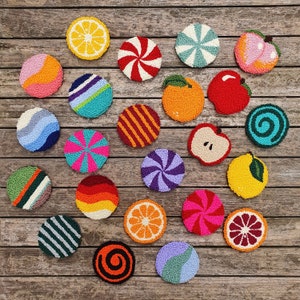 May include: A collection of 20 colorful, round, embroidered coasters with various designs, including fruit, candy, and geometric patterns. The coasters are arranged on a wooden surface.